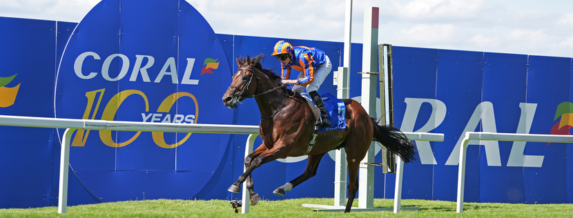 Horse and jockey in blue and orange riding gear jumping over a hurdle on a bright racetrack with a blue Coral banner in the background.